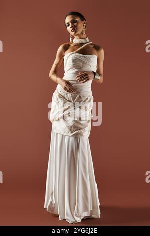 Une superbe déesse afro-américaine rayonne de beauté dans une robe blanche et un collier de perles sur un fond chaud. Banque D'Images