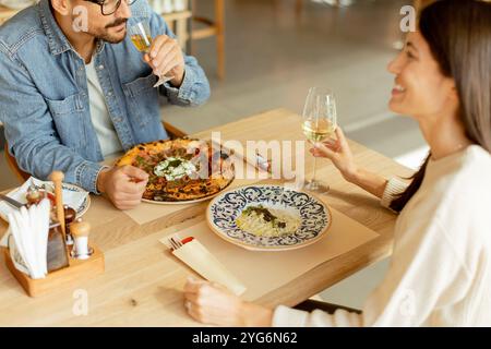 Deux personnes savourent leurs boissons à une table en bois, immergées dans une ambiance de restaurant détendue, tout en étant profondément dans la conversation et les rires. Banque D'Images