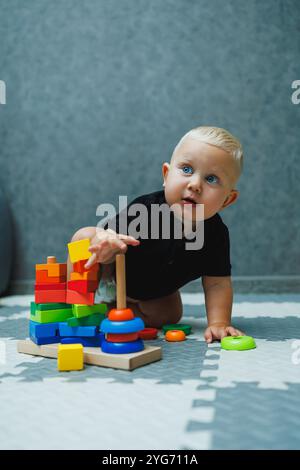 Un garçon en bas âge est assis sur un tapis et joue avec une pyramide en bois. Développement du bébé. Jouets pour bébés Banque D'Images