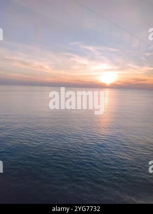 Un coucher de soleil à couper le souffle sur l'océan, où la lumière dorée chaude danse sur les vagues douces. Le ciel brille avec des nuances douces d'orange, de rose et de violet Banque D'Images