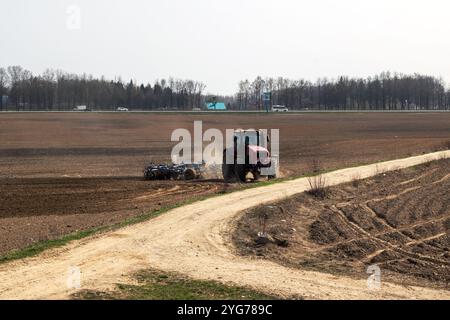 Un tracteur rouge vif laboure un grand champ le long d'un chemin de terre Banque D'Images