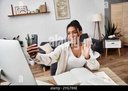 Une jeune femme aime étudier à la maison, interagissant joyeusement via son smartphone et son ordinateur portable. Banque D'Images