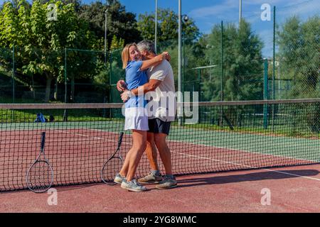 copyspace couple senior de joueurs de tennis partage triomphant câlin après avoir gagné leur match sur le court du club. Leurs expressions joyeuses et leur étreinte chaleureuse Banque D'Images