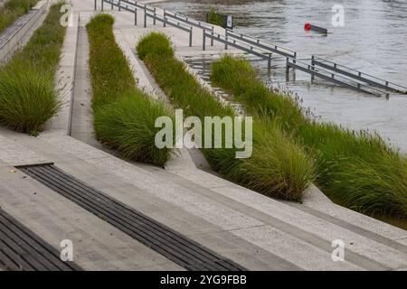 Promenade inondée au bord de la rivière avec des sentiers submergés et des herbes ornementales vertes dans la ville européenne après de fortes pluies Banque D'Images
