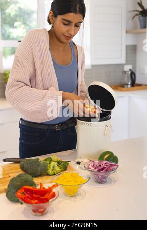 Femme asiatique compostant des restes de légumes dans la cuisine, favorisant un mode de vie écologique, à la maison Banque D'Images