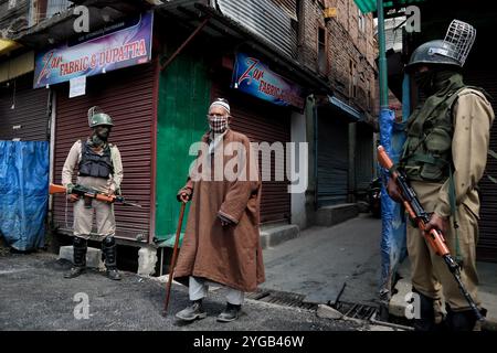 Un homme cachemirien marche alors que les troupes indiennes se tiennent devant la grande mosquée du Cachemire pendant le confinement du COVID-19 le dernier vendredi du Ramadan à Srinagar, au Cachemire sous administration indienne, le 7 mai 2021. Des milliers de personnes assistent aux prières les jours normaux chaque année en raison du covid-19. Toutes les mosquées principales ont été fermées. Banque D'Images