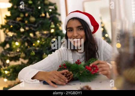 Femme souriante dans le chapeau de Père Noël fabriquant une couronne de Noël à la maison Banque D'Images