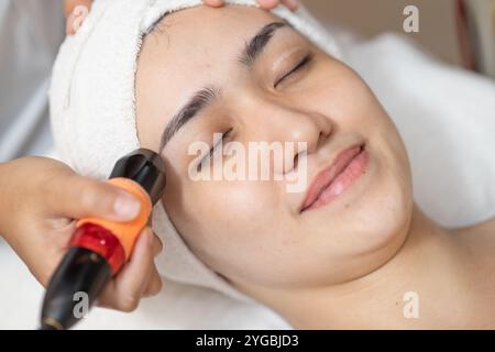 Le traitement de la peau du visage de belles femmes, le dispositif de massage ultrasonique pour le soulèvement facial activent le collagène et le resserrement de la peau dans le spa du salon de beauté. Banque D'Images