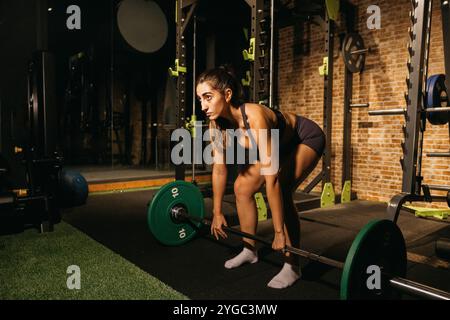 Une femme concentrée et déterminée exerce dans un gymnase, soulevant des poids dans le cadre de sa routine de musculation. Banque D'Images