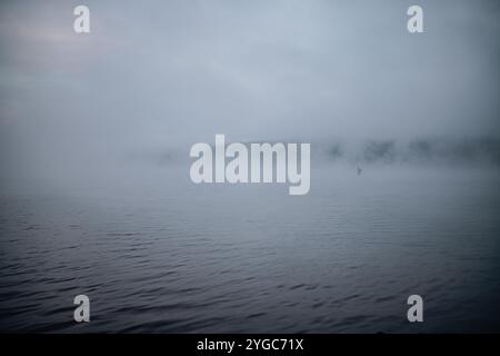 Tronc d'arbre solitaire dans la distance partiellement submergé dans les eaux ondulées du barrage Wellington. Un nuage bas crée un mystérieux brouillard matinal, obscuri Banque D'Images