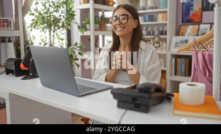 Jeune belle femme travaillant dans le magasin de décoration à la maison, souriant à l'ordinateur portable avec des articles de décoration intérieure en arrière-plan Banque D'Images