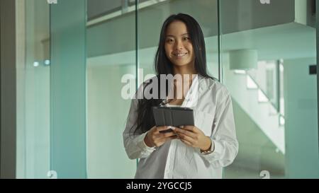 Attrayant, jeune, asiatique, femme, debout, intérieur, lieu de travail, tenir, tablette, sourire, en toute confiance. Banque D'Images