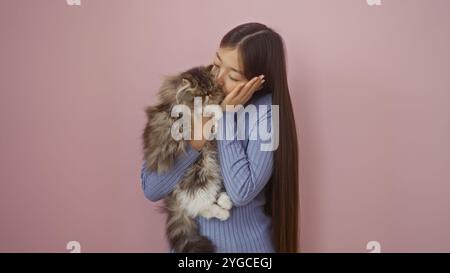 Une jeune femme chinoise câlin son chat à fourrure sur un fond rose, montrant un lien affectueux et tendre entre l'animal et le propriétaire. Banque D'Images