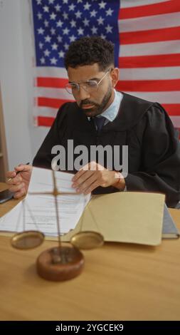 Juge lisant des documents au bureau avec drapeau américain, mettant en vedette un jeune homme sérieux travaillant dans le cadre d'une salle d'audience Banque D'Images