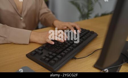 Une femme tape sur un clavier dans un cadre de bureau, montrant ses mains avec une bague en or, entourée de plantes d'intérieur et d'un bureau en bois. Banque D'Images