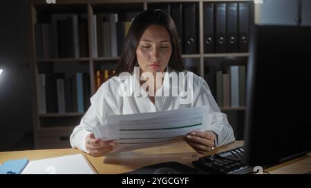 Jeune femme lisant des documents au bureau dans un cadre de bureau avec fond d'étagère pendant les heures de travail Banque D'Images