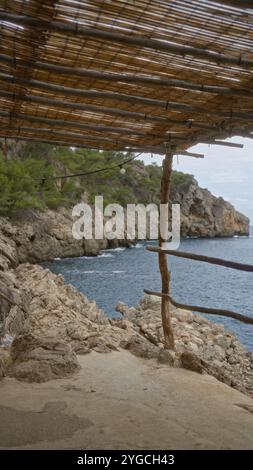 Belle vue sur la côte depuis un pavillon rustique en bois surplombant les falaises rocheuses et les eaux bleues de cala deia à majorque, en espagne, entouré de végétation luxuriante Banque D'Images