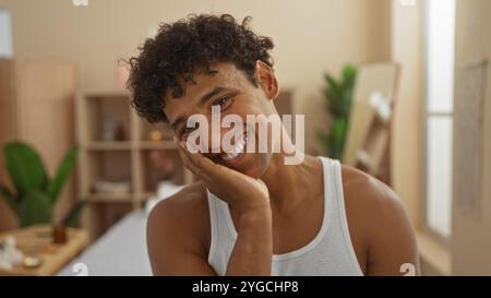 Jeune homme souriant chaleureusement dans une chambre spa tranquille au décor élégant, mettant en valeur l'ambiance bien-être et beauté. Banque D'Images