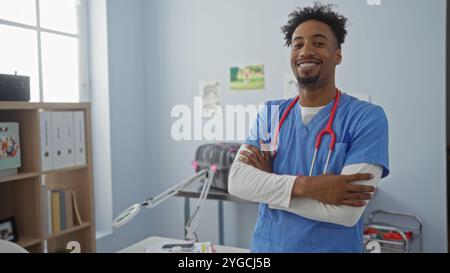 Un beau jeune homme afro-américain vétérinaire avec une barbe et les bras croisés se tient en toute confiance dans une clinique vétérinaire portant des gommages bleus, avec e médical Banque D'Images