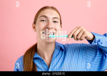 Fille avec des accolades nettoyant les dents sur fond rose Banque D'Images