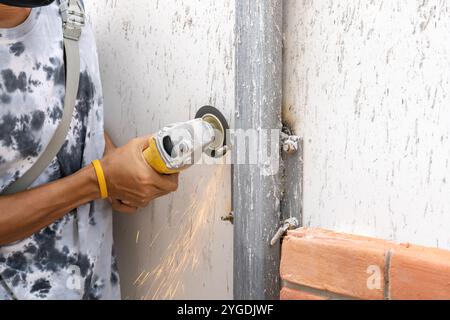 Un jeune travailleur asiatique sciait et conservait une vis métallique détaillée à partir d'un poteau en acier pour se préparer à installer un mur en brique de mousse. Banque D'Images