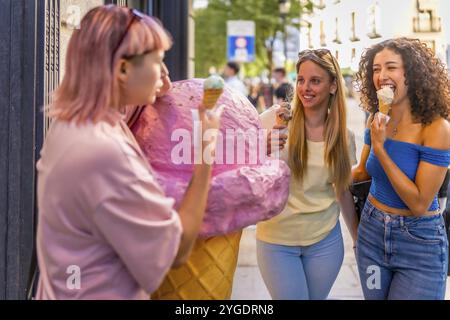 Les filles s'amusent à manger de la crème glacée dans la ville debout devant le magasin de crème glacée avec une figure géante d'un cône Banque D'Images