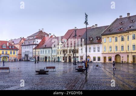 Sibiu, Roumanie, 27 mars 2015 : maisons avec de célèbres fenêtres en forme d'oeil sur les toits et les gens sur la place principale, Europe Banque D'Images