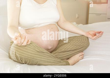 Femme enceinte méditant paisiblement sur un lit Banque D'Images