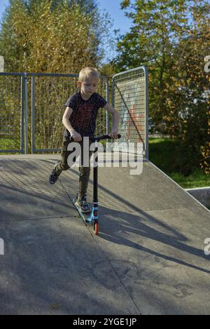 Garçon sur scooter fait un tour et profiter de son équitation dans le parc de skate au jour nuageux de printemps. Jeune homme faisant tour sur le scooter de kick dans le parc. Fu Banque D'Images