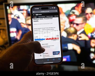 Paris, France - 6 novembre 2024 : gros plan téléphonique en direct des résultats des élections de CNN sur un téléphone portable montrant Donald Trump projeté comme vainqueur de la présidentielle 2024, avec une couverture télévisée en arrière-plan Banque D'Images