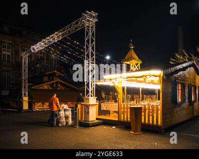 Strasbourg, France - 23 décembre 2024 : deux ouvriers nettoient près d'une stalle en bois vide et éclairée après les heures d'ouverture du marché de Noël de Strasbourg, soulignant l'entretien post-festival Banque D'Images