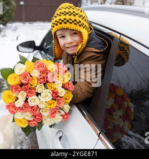 grand bouquet de nombreuses roses dans les mains d'un garçon regardant par la fenêtre de la voiture. Fête des mères. Journée internationale de la femme. Saint Valentin. Un agréable Banque D'Images