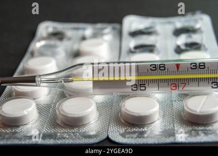 Image détaillée de pilules de paracétamol avec un thermomètre, mettant l'accent sur les soins de santé et le traitement du rhume / grippe, sur un fond sombre et contrasté. Banque D'Images