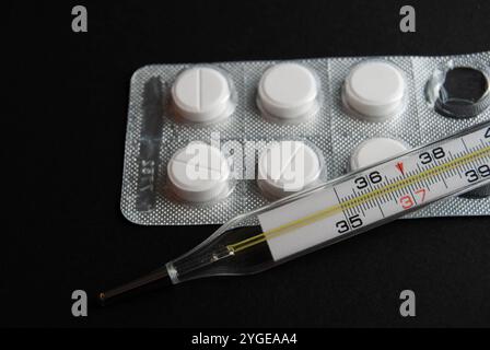 Concept médical avec des pilules de paracétamol et un thermomètre sur fond noir, parfait pour la saison de la grippe ou des thèmes de santé générale. Banque D'Images