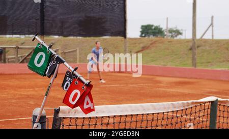 Tableau d'affichage sur un court de tennis en terre battue avec un joueur en arrière-plan Banque D'Images