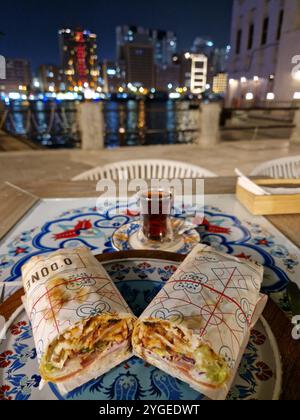 L'image capture une expérience gastronomique pittoresque dans la vieille ville de Deira, Dubaï, avec une table sertie avec un délicieux sandwich Doner Kebab et un verre de thé. Banque D'Images