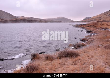 Évaporation s'élevant de la surface d'un beau lac dans les montagnes avec de la glace sur les rives par un matin nuageux d'automne. Banque D'Images