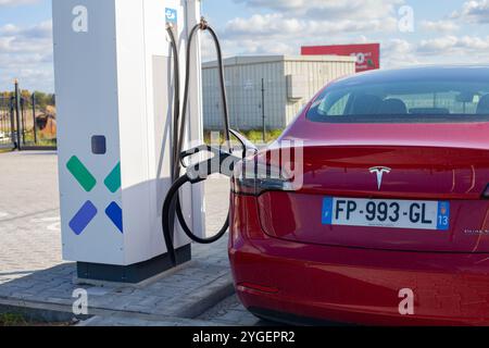 Voiture américaine entièrement électrique rouge Tesla Model 3 Dual Motor dans le parking avec station de charge rapide Banque D'Images