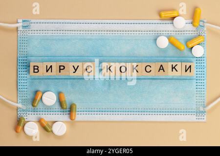 Вирус Коксаки - Coxsackievirus en russe, épelé avec des cubes en bois sur un masque chirurgical, entouré de pilules. Banque D'Images