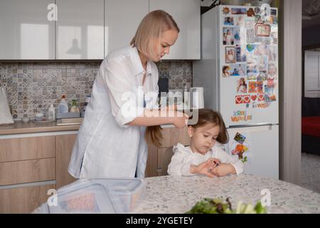 Mère aidant sa fille à se préparer à l'école dans la cuisine Banque D'Images