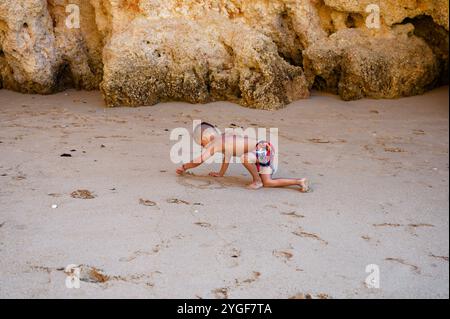 Jeune garçon concentré sur le dessin dans le sable à praia da rocha, profitant d'un moment tranquille de créativité Banque D'Images