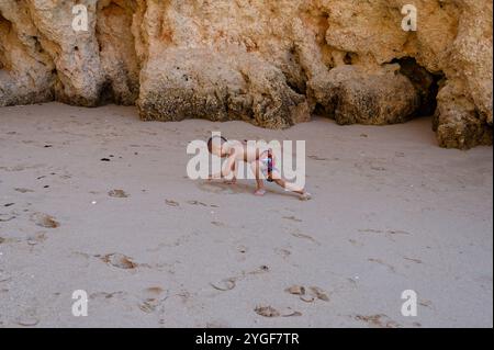 Jeune garçon concentré sur le dessin dans le sable à praia da rocha, profitant d'un moment tranquille de créativité Banque D'Images