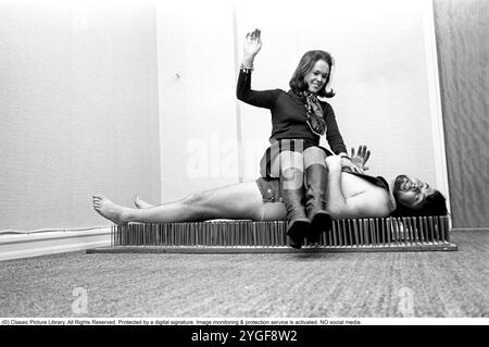 Un fakir repose sur un tapis de clous. Le fakir suédois Mr. Swing, de son vrai nom Kjell Swing (1942-1988). L’artiste et chanteuse Gunilla af Halmstad est assise sur lui mais cela ne semble pas le déranger du tout. 1969 Banque D'Images