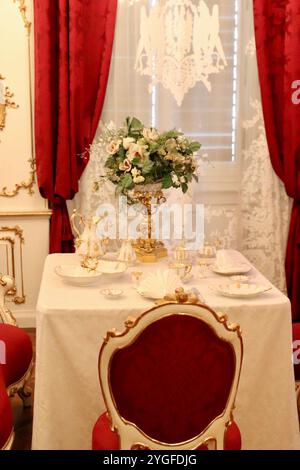 Vienne, Autriche - 6 octobre 2024 : élégante salle à manger Vintage dans le palais de Schönbrunn avec des chaises en velours rouge ornées, ensemble en porcelaine ornée, et Banque D'Images