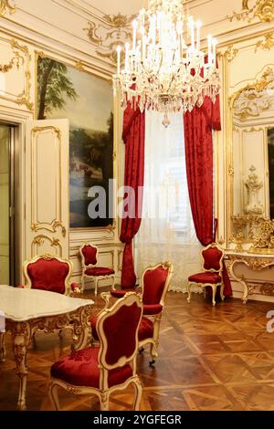 Vienne, Autriche - 6 octobre 2024 : somptueuse salle rococo au Palais Schönbrunn avec chaises en velours rouge, table en marbre, détails dorés et lustre en cristal Banque D'Images