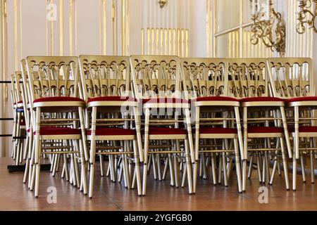 Vienne, Autriche - 6 octobre 2024 : chaises dorées empilées avec coussins en velours rouge dans le cadre de la salle de bal ornée du palais de Schönbrunn. Photo de haute qualité Banque D'Images