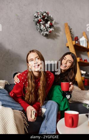 Deux copines en chandails confortables apprécient la compagnie de l'autre et célèbrent la saison des fêtes à la maison. Banque D'Images