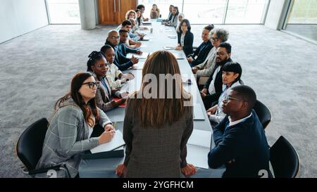 Une dirigeante s'adressant à une équipe d'affaires diversifiée dans une salle de conseil lors d'une réunion, favorisant le leadership et le travail d'équipe. Banque D'Images