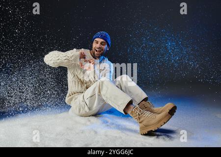 Un jeune homme en tenue d'hiver crée de manière ludique une forme de coeur avec ses mains dans la neige. Banque D'Images