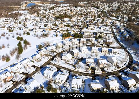 C'est un paysage de banlieue américain enneigé avec des lignes claires de bâtiments, des routes, des arbres dispersés dans un cadre hivernal serein. Banque D'Images